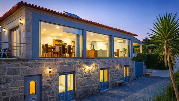 A modern house with large windows, stone walls, and a cobblestone driveway.
