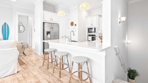 Uma cozinha moderna com armários brancos, uma ilha central com banquetas e iluminação pendente.