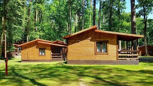 Eine Reihe von Holzhütten mit überdachter Veranda und kleiner Terrasse, umgeben von einem Wald.