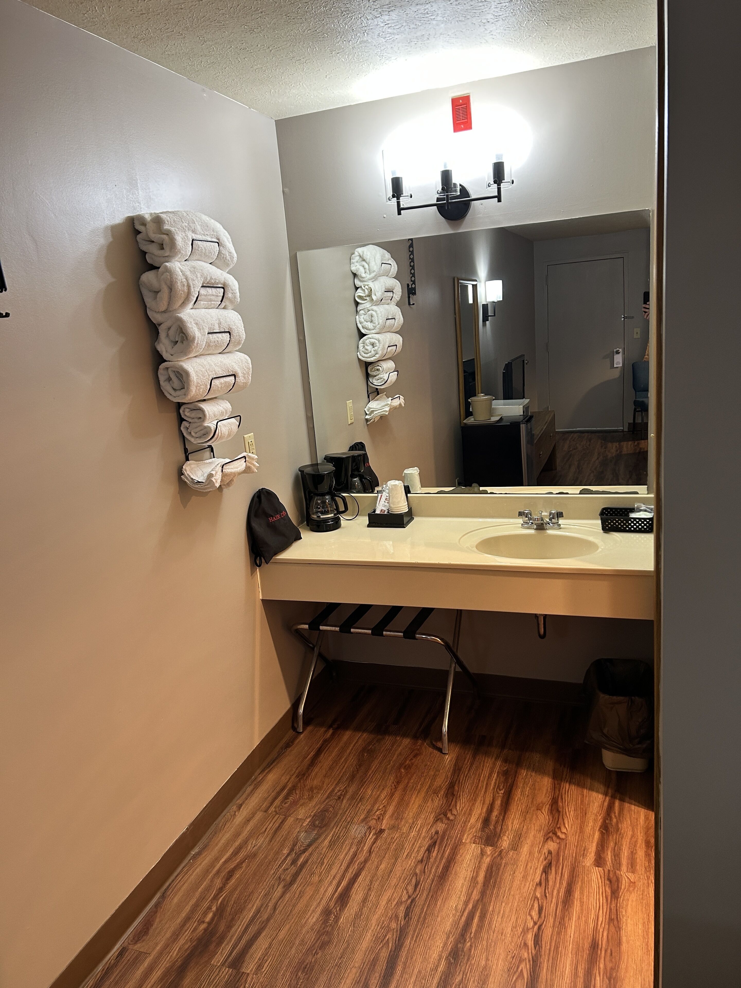 Un baño de hotel con suelo de madera, un lavabo, un espejo y toallas colgadas en la pared.