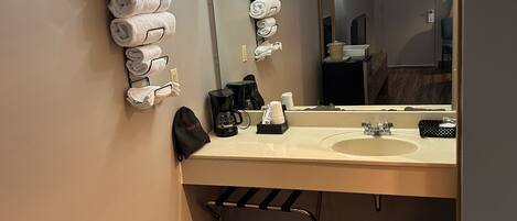 Un baño de hotel con suelo de madera, un lavabo, un espejo y toallas colgadas en la pared.
