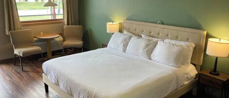 A hotel room with a large bed, two bedside tables with lamps, a chair, and a view of a building through a window.