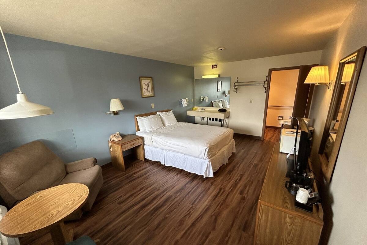 Ein Hotelzimmer mit einem Bett, einem Schreibtisch, einem Sessel, einem kleinen Tisch, einem Spiegel und einem Nachttisch.