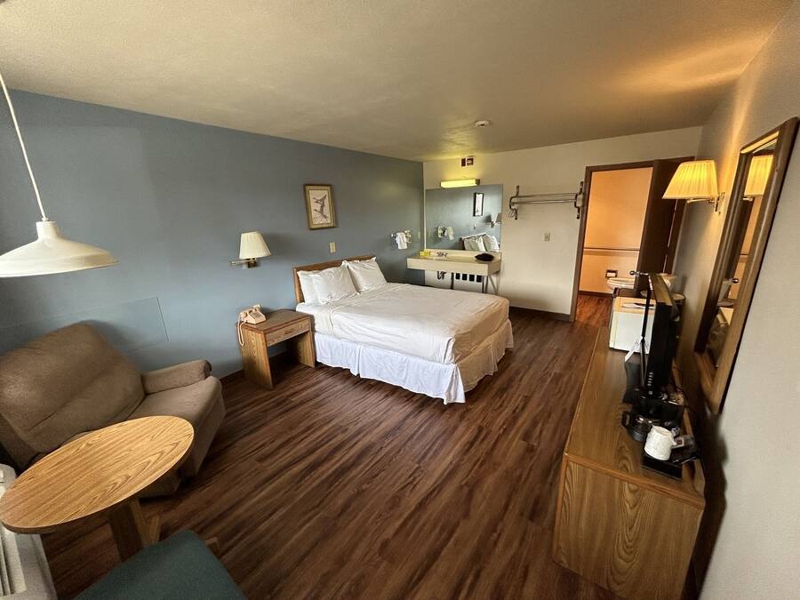 A hotel room with a bed, a desk, a chair, a small table, a mirror, and a nightstand.