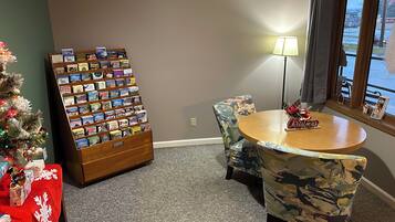 A hotel room with a Christmas tree, a book display, a round table with a 'Christmas' sign, and a view of the outside through a window.