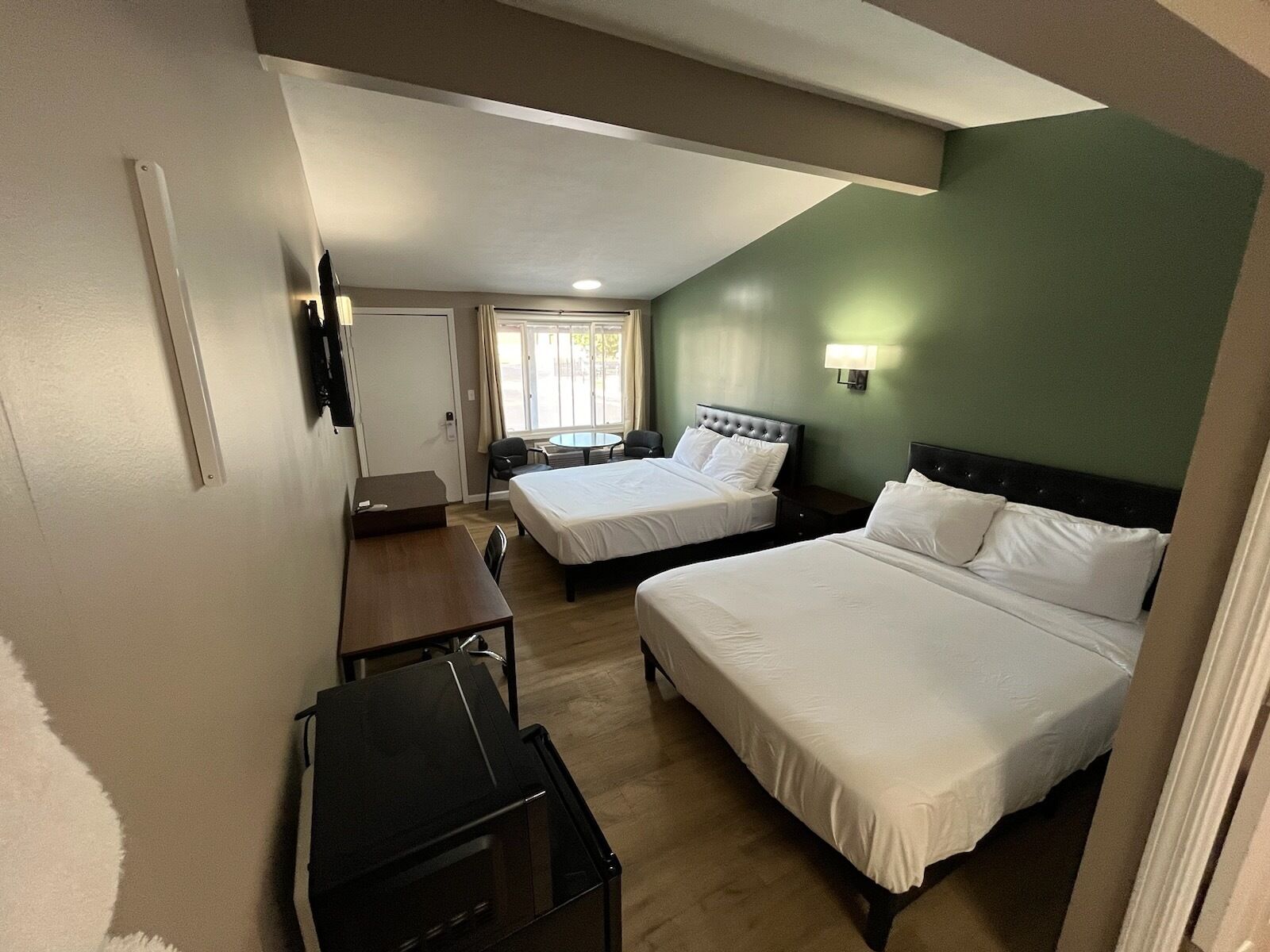 A hotel room with two beds, a desk, a chair, a TV, and a window with curtains.