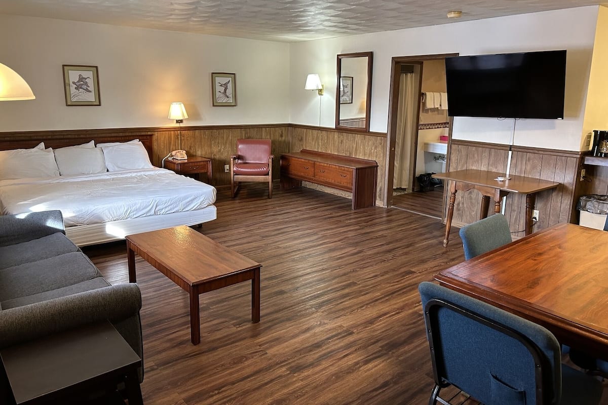 Ein Hotelzimmer mit einem Bett, einem Schreibtisch, einem Sessel, einer Couch, einem Fernseher und Holzböden.