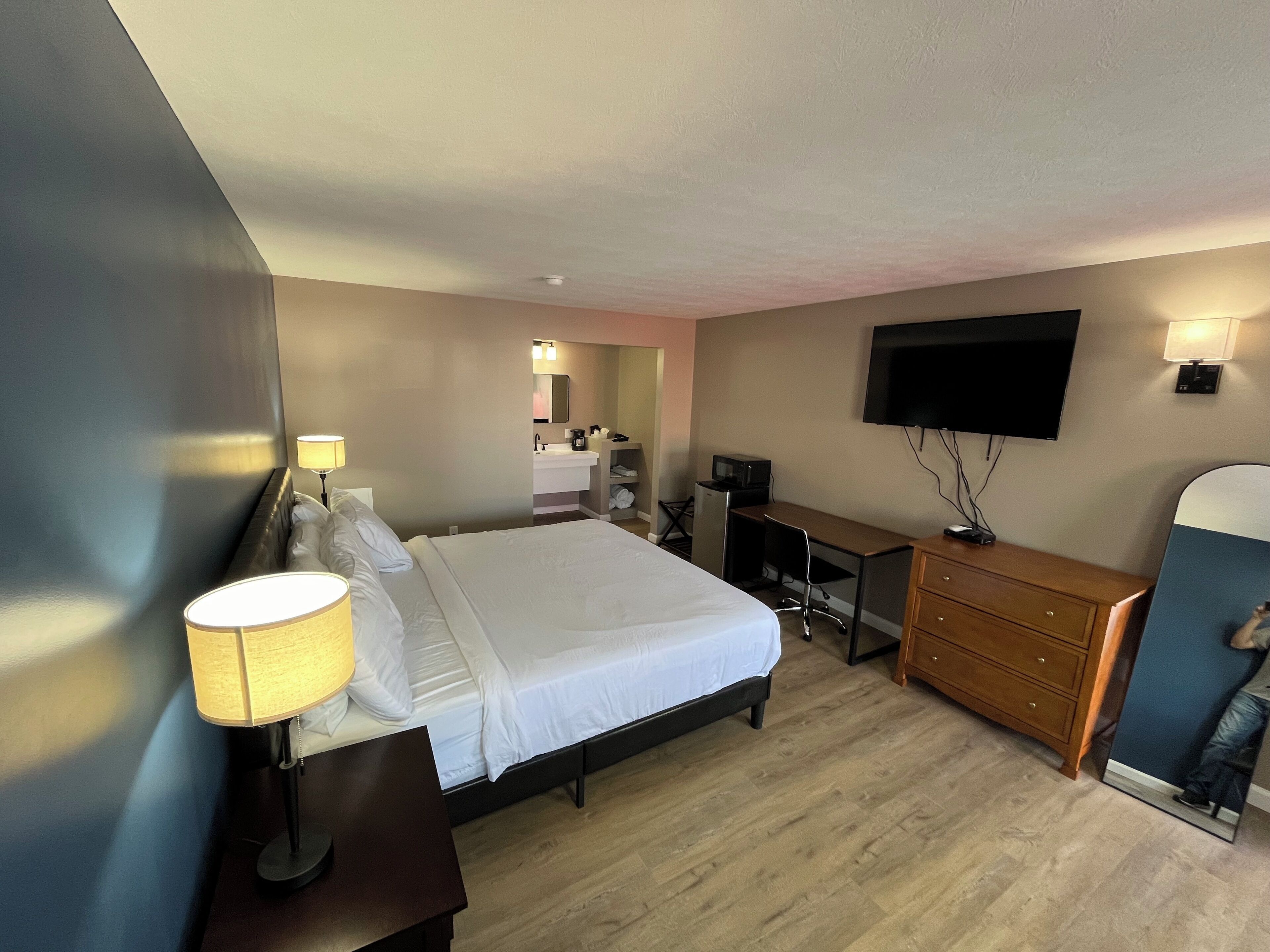 A hotel room with a bed, desk, dresser, TV, and a mirror.