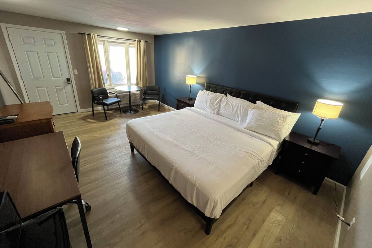 Ein Hotelzimmer mit einem Bett, zwei Nachttischen mit Lampen, einem Schreibtisch und einem Sessel.