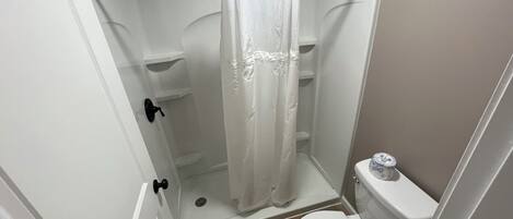 A small, enclosed shower area with a white shower curtain, a toilet, and a wooden floor.