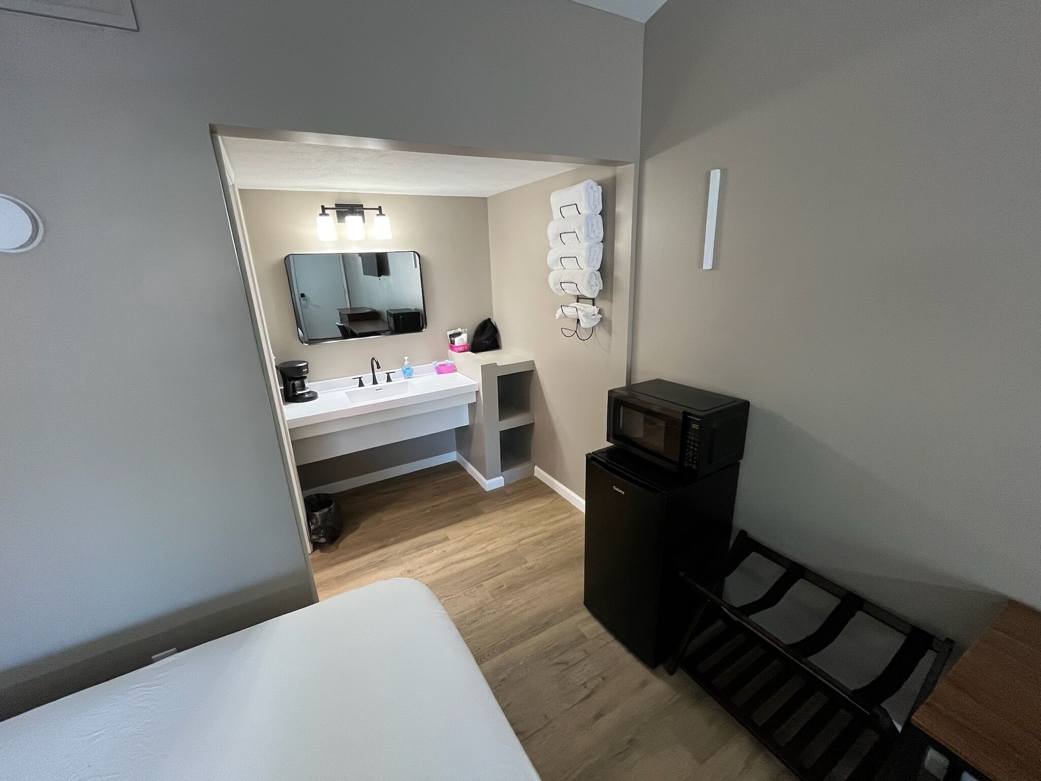 Habitació d'hotel senzilla i compacta amb un llit individual, una cuineta petita que inclou microones, un rentaplat i un mirall.