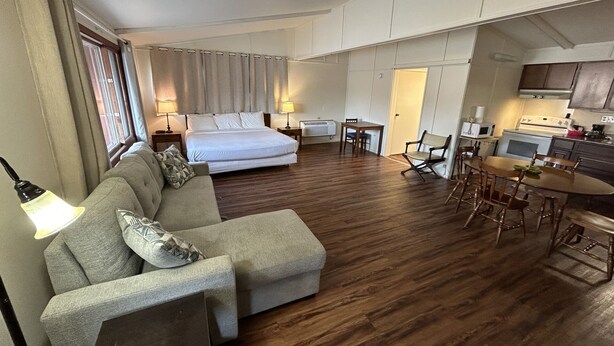A hotel room with a bed, a sofa, a dining table with chairs, a kitchen area, and a window with curtains. - Valley Inn and Suites (French Lick)