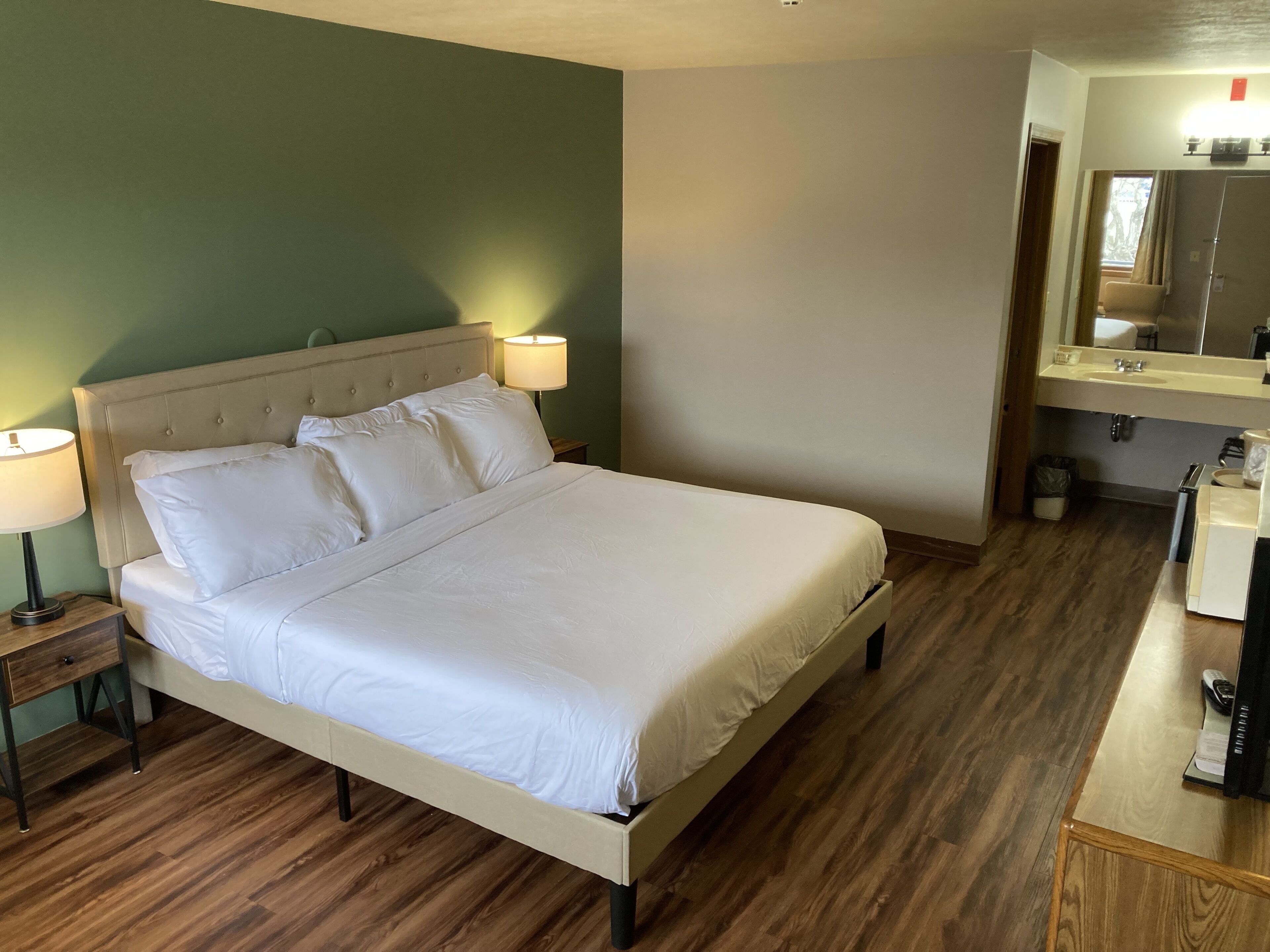 A neatly made bed with white linens in a room with wooden flooring and a green accent wall.