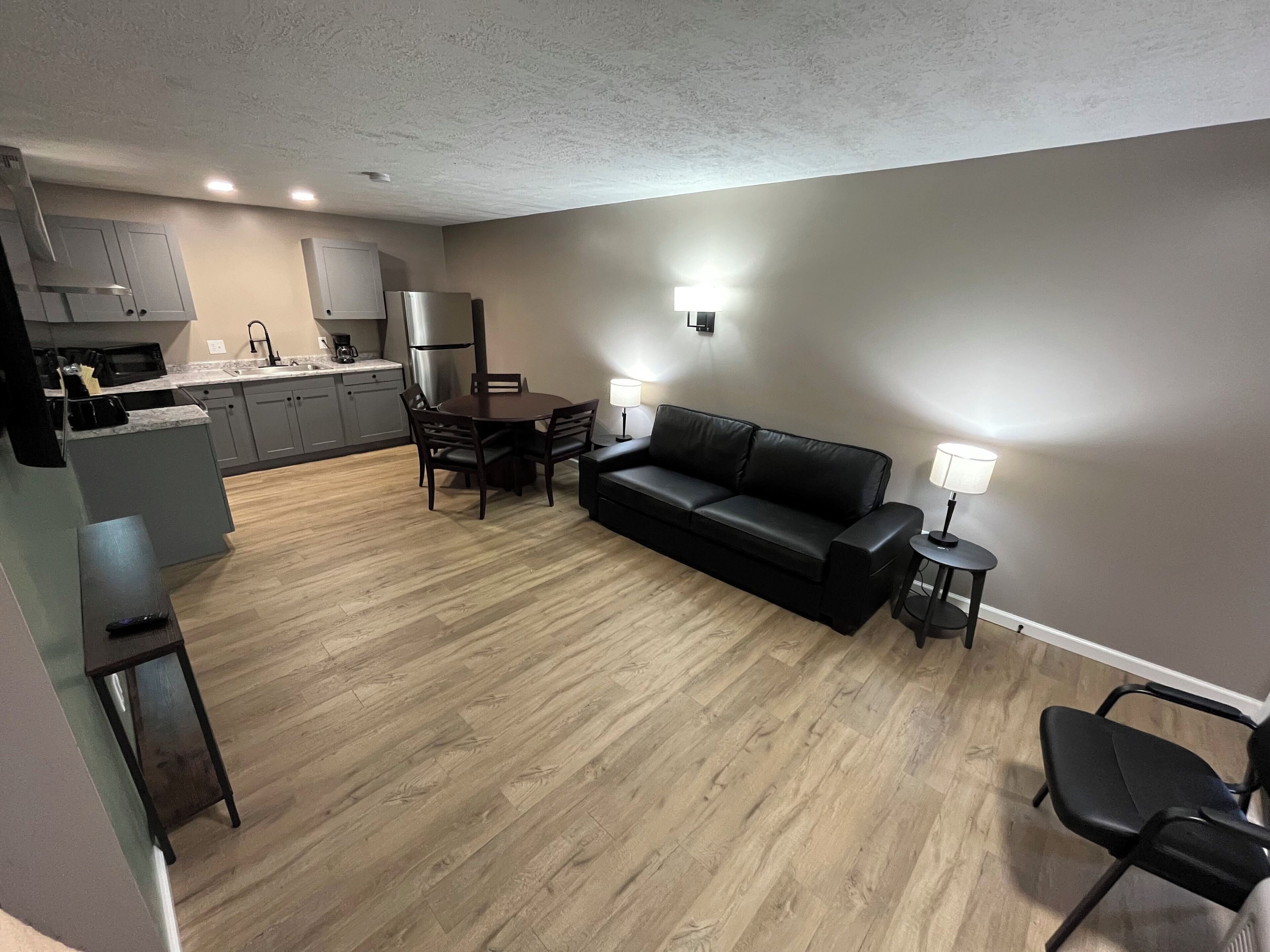 Un espacio habitable compacto con kitchenette, comedor y zona de estar con sofá y sillones.