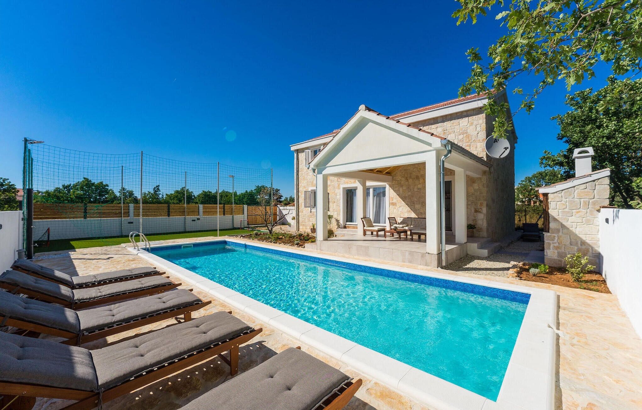 A swimming pool with lounge chairs, a covered patio, and stone walls.