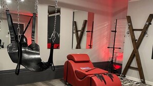 Una habitación con una silla de masajes, una hamaca colgante y una estructura de madera en forma de X.