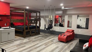 Un dormitorio moderno con una litera, una silla colgante, un sofá rojo y una pequeña kitchenette.