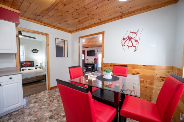A dining area with a glass table and red chairs, a wooden ceiling, and a white wall with a red abstract design.
