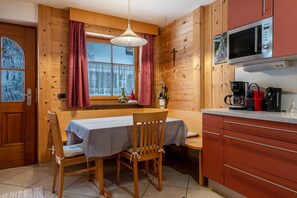 Een houten interieur met een eettafel, stoelen, een raam met gordijnen, een magnetron en een koffiezetapparaat.