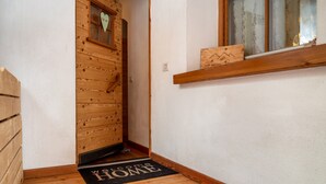 Une porte en bois ornée d’une fenêtre en forme de cœur, un paillasson sur lequel est écrit « BIENVENUE CHEZ VOUS », et un rebord de fenêtre sur lequel repose une boîte en bois.