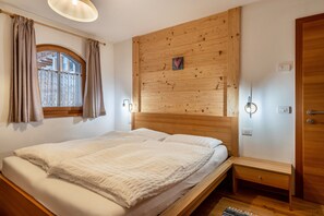 Une chambre avec une tête de lit en bois, une fenêtre avec des rideaux, une table de chevet et un plancher en bois.