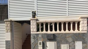 Ein Gebäudeeingang mit einer Steinmauer, einem Metallgitter und einer Treppe zu einem überdachten Bereich.