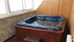 Ein Whirlpool mit Stufen, vor einer Holzwand und einer Steinwand, mit einem Fenster auf der linken Seite.