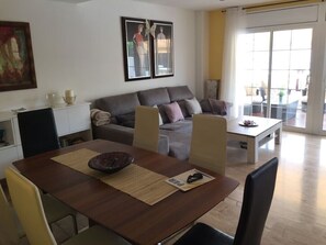 Un salon moderne avec un canapé, une table à manger et des chaises. Une grande fenêtre laisse entrer la lumière naturelle et offre une vue sur l’extérieur.