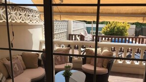 Ein Balkon mit Korbmöbeln, einem Glastisch und Blick auf den Pool und die Grünanlage.