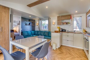 A modern kitchen with a dining area, a built-in sofa, and a small island with a sink. - Mobile Home 'Le 370' with Shared Pool, Private Terrace and Private Garden Lattes (Lattes)