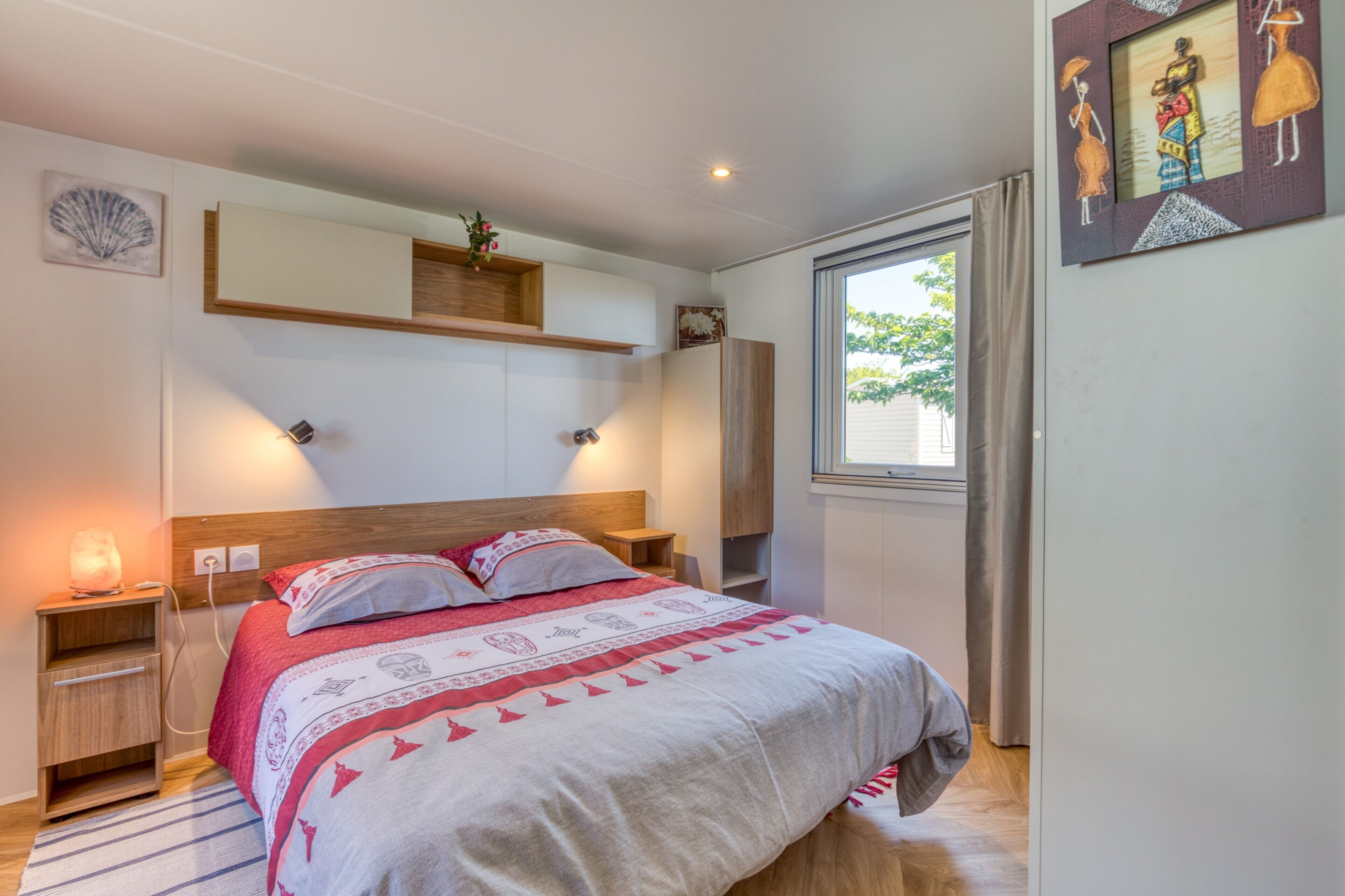Une chambre à coucher comprenant un lit, des tables de chevet, une commode, une fenêtre et des œuvres d’art accrochées aux murs.