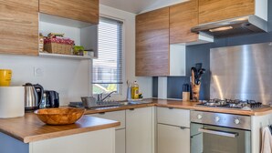 A modern kitchen with wooden cabinets, a stainless steel refrigerator, a gas stove, and a built-in oven. - Mobile Home 'Le 370' with Shared Pool, Private Terrace and Private Garden Lattes (Lattes)