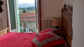 Ein Schlafzimmer mit einem großen Bett, Blick auf ein Gebäude mit rotem Dach, einem Heizkörper und einer hölzernen Kommode.