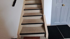 Eine Treppe mit Teppichstufen, einem schwarzen Geländer, einer Tür mit Knauf und einem kleinen Fenster am oberen Ende.