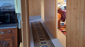 Ein Flur mit Holzwänden, eine Küchenzeile mit Mikrowelle, ein gemustertes Teppich und ein Bett mit farbenfroher Decke.