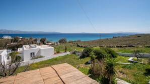 A coastal property with a wooden deck, white buildings, and a view of the sea. - Holiday Home 'Punda Beach Seaside Retreat' with Sea View, Wi-Fi and Air Conditioning (Paros)