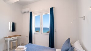 A bedroom with a bed, a desk, a chair, a mirror, and a window with curtains. - Holiday Home 'Punda Beach Seaside Retreat' with Sea View, Wi-Fi and Air Conditioning (Paros)