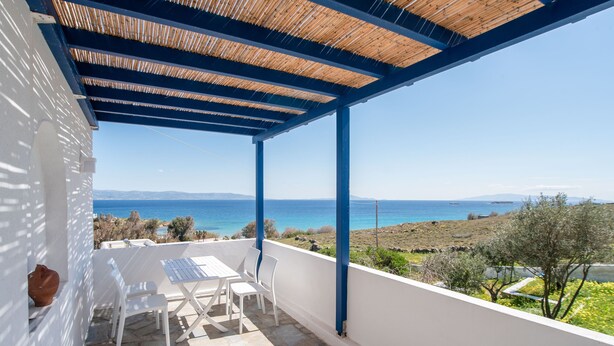 A covered outdoor seating area with a table and chairs, overlooking a coastal landscape. - Holiday Home 'Punda Beach Seaside Retreat' with Sea View, Wi-Fi and Air Conditioning (Paros)