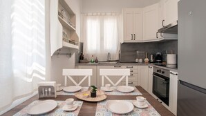 A modern kitchen with white cabinets, a dining table set with plates, cups, and a small plant centerpiece. - Holiday Home 'Punda Beach Seaside Retreat' with Sea View, Wi-Fi and Air Conditioning (Paros)