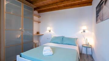A bedroom with a bed, two wall-mounted lamps, a wardrobe with frosted glass doors, and a wooden ceiling.