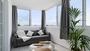 Ein modernes Wohnzimmer mit einem grauen Sofa, einem weißen Pouf und einer großen Kübelpflanze.
