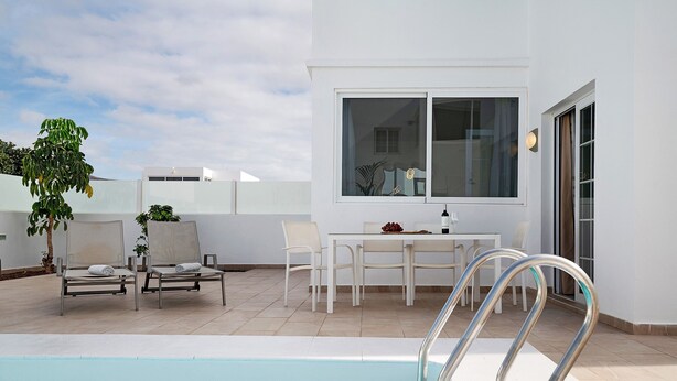 Ein Poolbereich mit einem klaren, blauen Pool, weißen Liegestühlen, einem Tisch mit Stühlen und einem Fenster mit Blick auf den Pool.