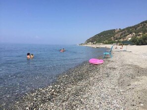 A pebbly beach with clear water, a few people swimming, and a pink inflatable on the shore. - Apartment 'Tenuta Baronale Jò - Sant'elia 4' with Sea View, Shared Terrace (Palizzi Marina)