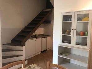 Un escalier menant à une cuisine équipée de meubles de rangement et d’un meuble blanc aux portes vitrées.