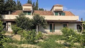 Un edificio de dos pisos con techo de tejas, contraventanas verdes y un jardín delantero.