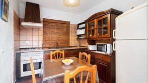 A kitchen with a stove, microwave, wooden cabinets, and a dining table with chairs. - Apartment 'Trebol 3' with Sea View, Private Terrace and Wi-Fi (El Mocanal)