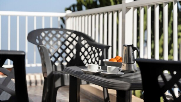 A table with two white cups and a silver coffee pot, surrounded by black chairs on an outdoor deck with a white railing and green plants in the background. - Apartment 'Trebol 3' with Sea View, Private Terrace and Wi-Fi (El Mocanal)