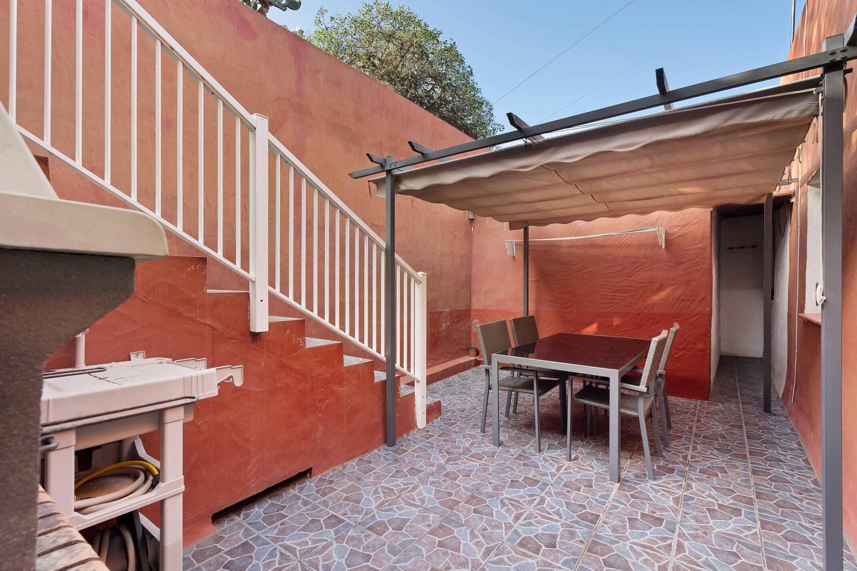 A covered patio area with a table and chairs, a white railing, and a tiled floor.