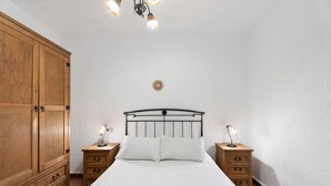 A bedroom with a large wooden wardrobe, a metal bed frame, two bedside tables with lamps, and a plain white wall. - Apartment 'Trebol 3' with Sea View, Private Terrace and Wi-Fi (El Mocanal)