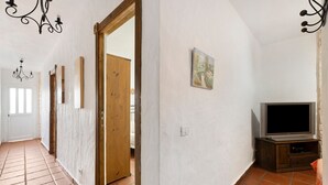 A hallway with a tiled floor, a wooden door, a white wall with a painting, and a television on a wooden stand. - Apartment 'Trebol 3' with Sea View, Private Terrace and Wi-Fi (El Mocanal)